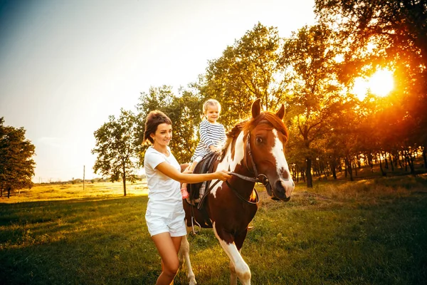 Liten flicka som rider på en häst med mamman promenader i närheten. — Stockfoto