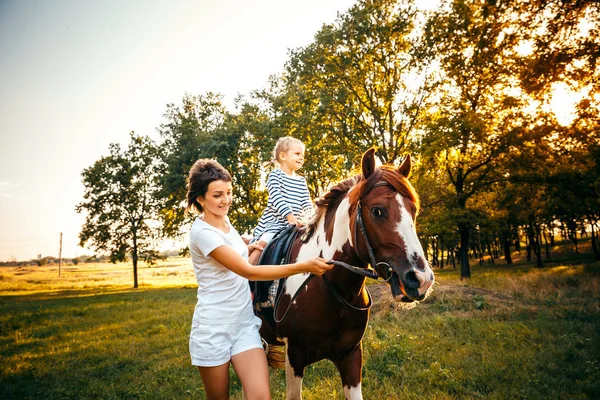 Menina montando em um cavalo com sua mãe andando nas proximidades . — Fotografia de Stock