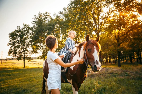 Menina montando em um cavalo com sua mãe andando nas proximidades . — Fotografia de Stock