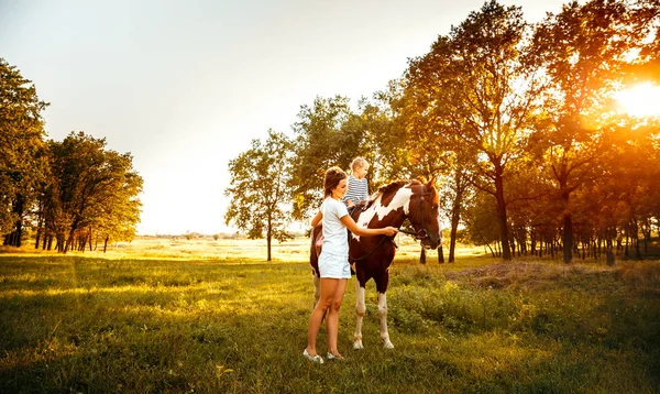 Маленька дівчинка їде на коні з матір'ю, що стоїть поруч . — стокове фото