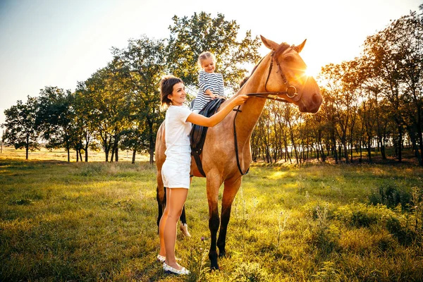 Menina montando em um cavalo com sua mãe de pé nas proximidades . — Fotografia de Stock