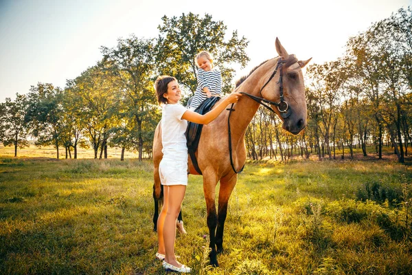 Menina montando em um cavalo com sua mãe de pé nas proximidades . — Fotografia de Stock