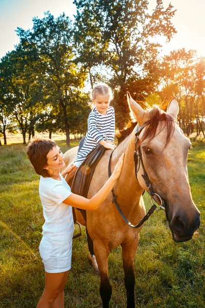 Маленькая девочка едет верхом на лошади со своей матерью, стоящей рядом . — стоковое фото