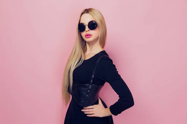 Portrait of young beautiful slim sexy young blonde woman in black sexy dress with red sensual lips on pink background in studio wearing sunglasses — Stock Photo, Image