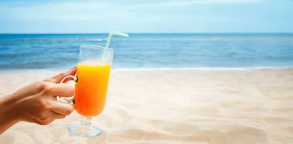 Hand holding Juice in a glass on blurred seascape background