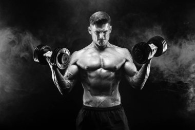 Yakışıklı vücut dumbbell egzersiz yapıyor. Stüdyo vurdu. Siyah ve beyaz fotoğraf. Duman