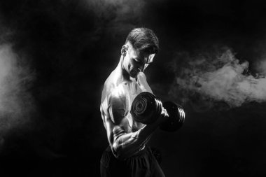 Yakışıklı vücut dumbbell egzersiz yapıyor. Stüdyo vurdu. Siyah ve beyaz fotoğraf. Duman