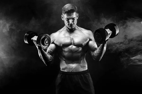 Yakışıklı vücut dumbbell egzersiz yapıyor. Stüdyo vurdu. Siyah ve beyaz fotoğraf. Duman — Stok fotoğraf