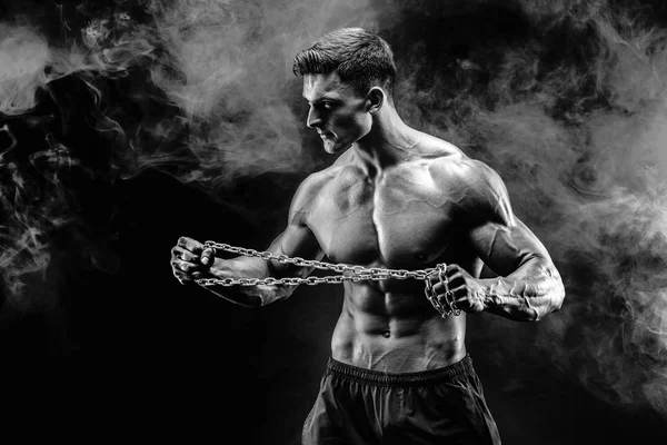 金属チェーンを引き裂く筋肉スポーツマンの肖像画。煙が黒の背景 — ストック写真