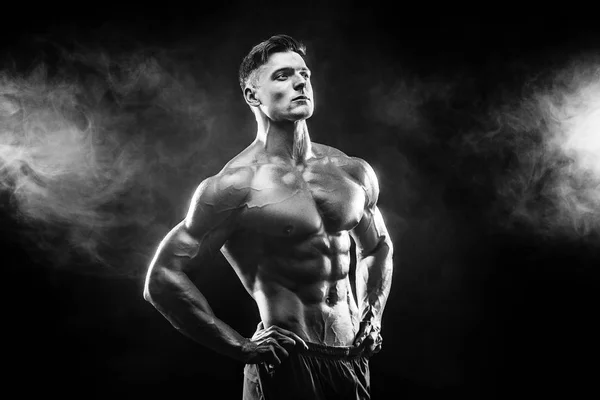 Ισχυρή bodybuilder άνθρωπος με τέλειο σώμα-abs, δικέφαλου, τρικέφαλος μύς, ώμους, στήθος θέτοντας σε φόντο καπνού στούντιο — Φωτογραφία Αρχείου