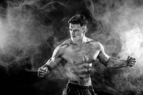 Strong bodybuilder man with perfect body- abs, shoulders, biceps, triceps, chest posing in studio smoke background