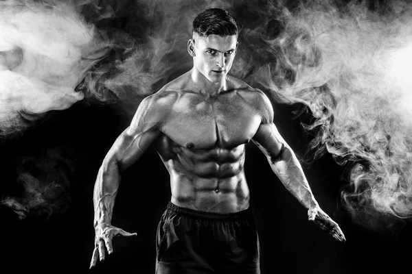 Homme bodybuilder fort avec le corps parfait- abdos, épaules, biceps, triceps, poitrine posant en arrière-plan de fumée de studio — Photo