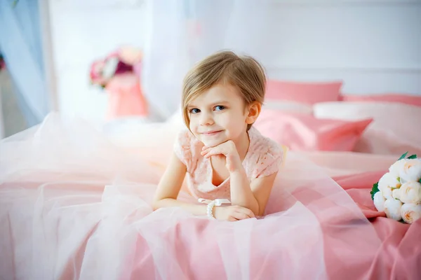 Pequena menina agradável no vestido deitado na cama com flores — Fotografia de Stock