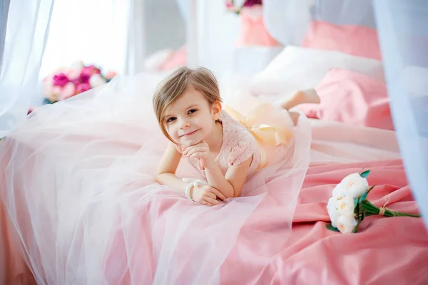 Kleines nettes Mädchen im Kleid, das auf dem Bett mit Blumen liegt — Stockfoto