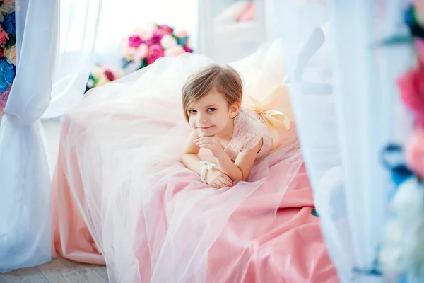 Kleines nettes Mädchen im Kleid, das auf dem Bett mit Blumen liegt — Stockfoto