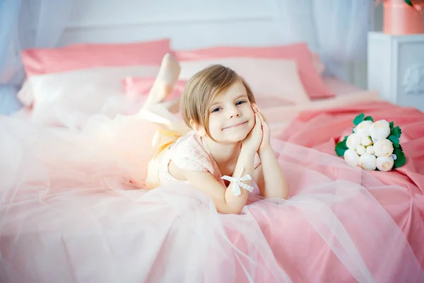 Маленькая симпатичная девочка в платье, лежащая на кровати с цветами — стоковое фото