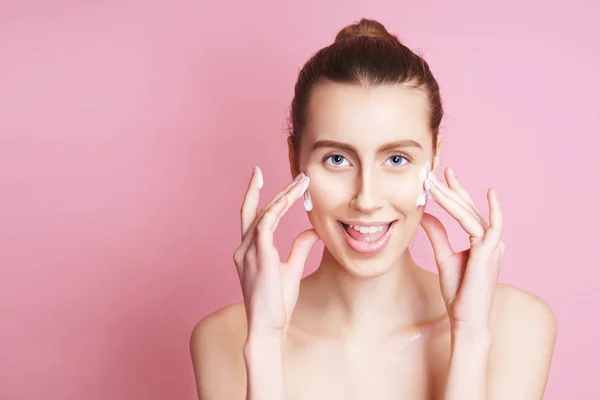 Portret van een dame van mooie model met natuurlijke make-up toe te passen crème op haar gezicht. geïsoleerd op roze — Stockfoto