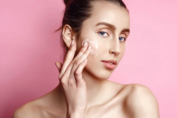 Gyönyörű modell hölgy natúr smink alkalmazása krém arcán portréja. elszigetelt rózsaszín — Stock Fotó