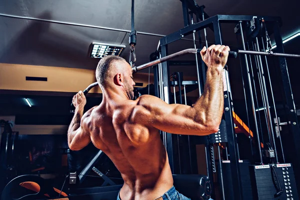 Arka üstünde makine için ağır egzersiz yaparak güçlü vücut geliştirmeci