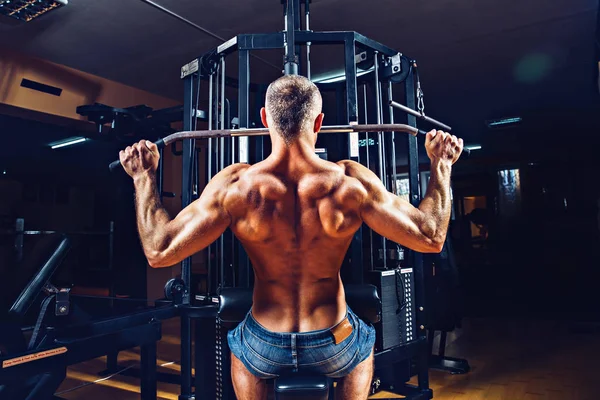 O halterofilista forte que faz o exercício pesado para trás na máquina — Fotografia de Stock