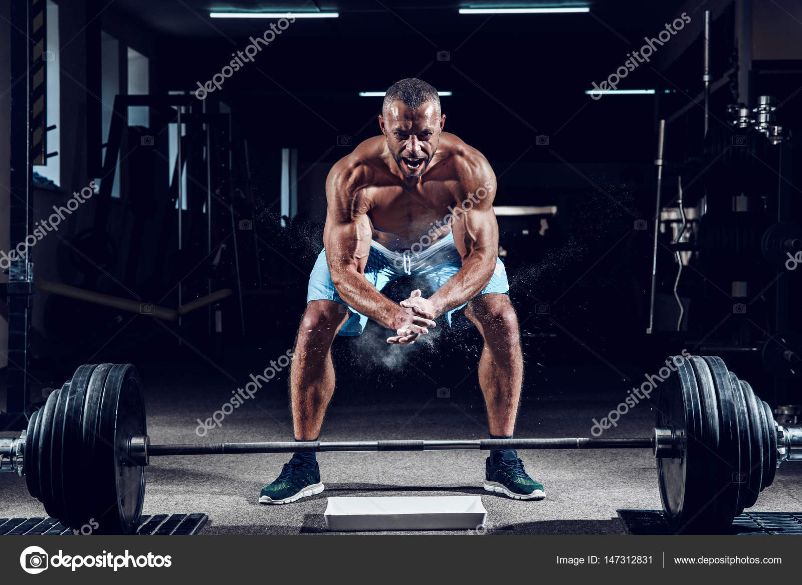 Muscular weightlifter clapping hands and preparing for workout at a gym. Screaming for