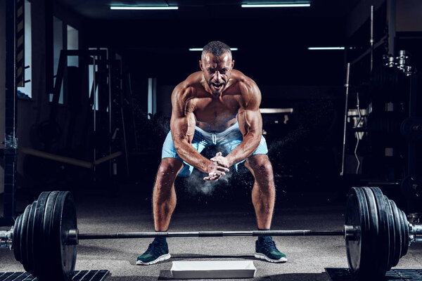 Muscular weightlifter clapping hands and preparing for workout at a gym. Screaming for motivation