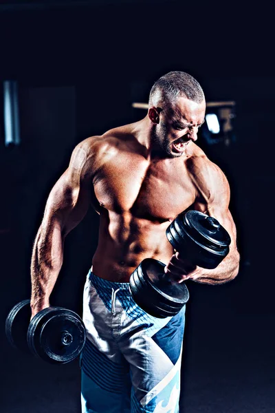 Retrato de un joven en el gimnasio, ejercicio para los bíceps. Blanco y negro. Lente de bengala. Baja luz —  Fotos de Stock