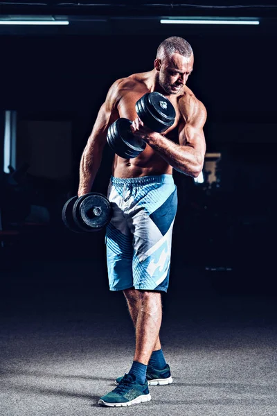 Retrato de un joven en el gimnasio, ejercicio para los bíceps. Blanco y negro. Lente de bengala. Baja luz —  Fotos de Stock