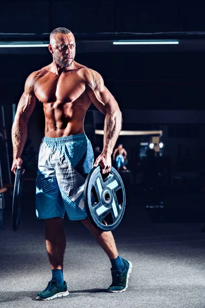 Power athletic guy standing in gym with dumbbells — Stock Photo, Image