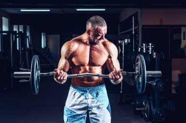 Spor salonunda büyük dumbbell ile pazı egzersizleri yaparken kas vücut geliştirmeci adam