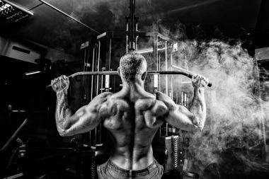 Güçlü vücut geliştirmeci için makine arkasında ağır egzersiz yapmak. Arka plan üzerinde duman