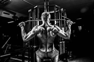 Arka üstünde makine için ağır egzersiz yaparak güçlü vücut geliştirmeci