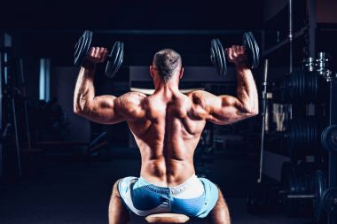 Kaslı adam omuzlarını spor salonunda dumbbells ile eğitim