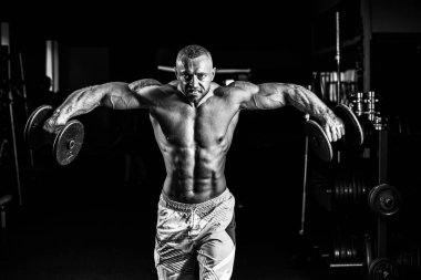 Kaslı adam omuzlarını spor salonunda dumbbells ile eğitim