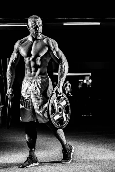 Power athletic guy standing in gym with dumbbells — Stock Photo, Image