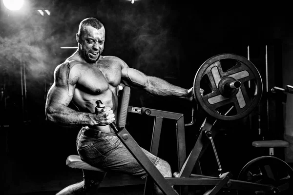 Culturista fuerte haciendo ejercicio de peso pesado para volver a la máquina. Humo en el fondo —  Fotos de Stock