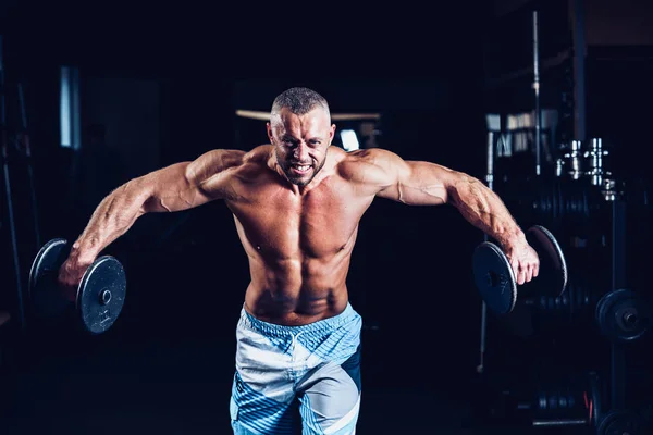 Мускулистый мужчина тренирует плечи гантелями в спортзале — стоковое фото