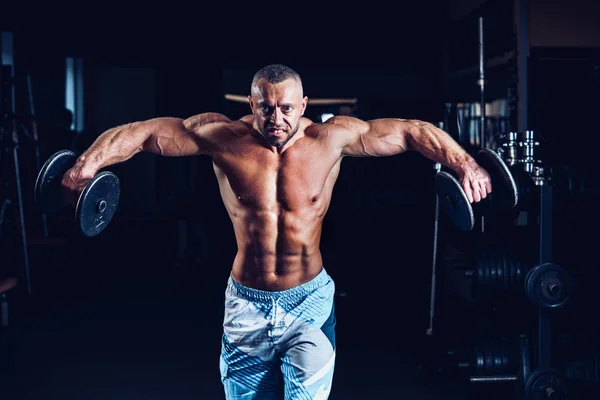 Musculoso hombre entrenando sus hombros con pesas en el gimnasio — Foto de Stock