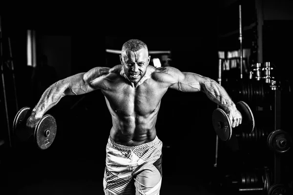 Musculoso hombre entrenando sus hombros con pesas en el gimnasio —  Fotos de Stock