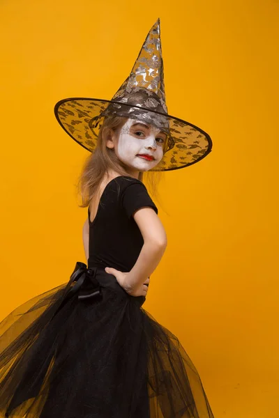 Menina pequena no traje de bruxa de Halloween, fundo laranja . — Fotografia de Stock