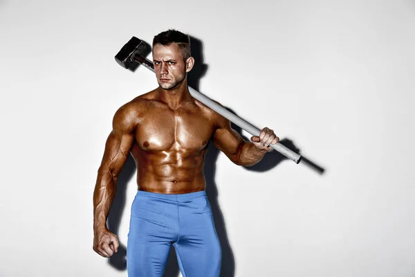 A sportoló és a kalapács. a srác egy szép izom fitness, testépítő tartsa nagy fém kalapács — Stock Fotó