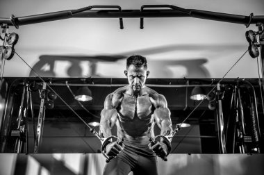 Genç vücut geliştirici, spor salonunda kablolu TV ile göğsü üzerinde çalışıyor.