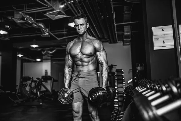 Hombre musculoso guapo está haciendo ejercicio y posando con pesas en un gimnasio — Foto de Stock