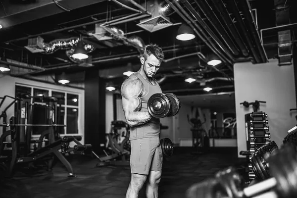 Hombre musculoso guapo está haciendo ejercicio y posando con pesas en un gimnasio —  Fotos de Stock