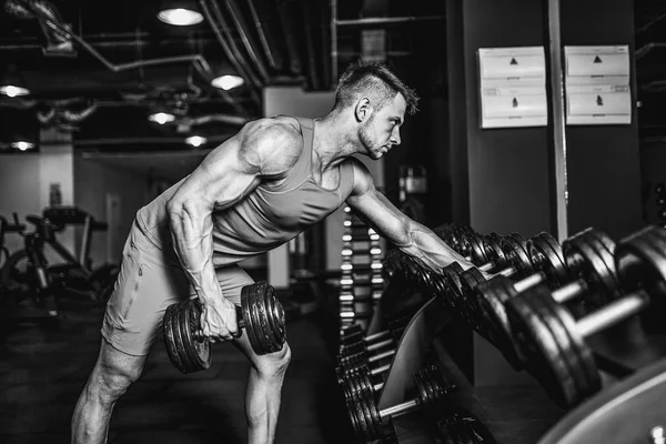 Hombre musculoso guapo está haciendo ejercicio y posando con pesas en un gimnasio — Foto de Stock