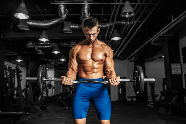 Jeune beau caucasien bodybuilder sportif travaillant avec un haltère dans la salle de gym, faire de l'entraînement biceps . — Photo