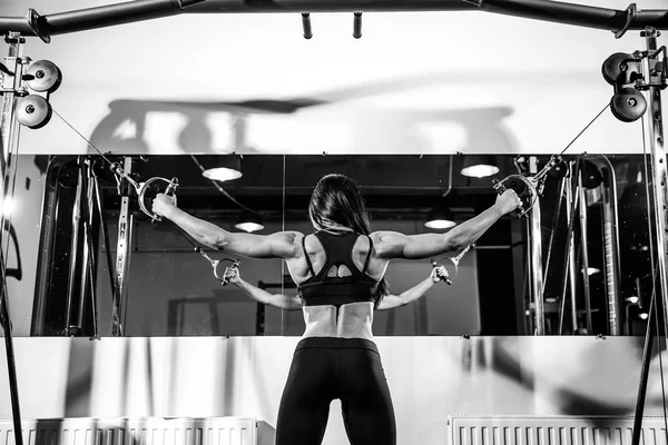 Mujer flexionando los músculos en la máquina de cable en el gimnasio. ejercicio en bíceps. vista posterior — Foto de Stock