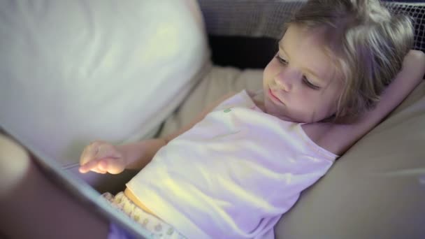 Niña linda sentada en el sofá y jugando con la tableta — Vídeo de stock