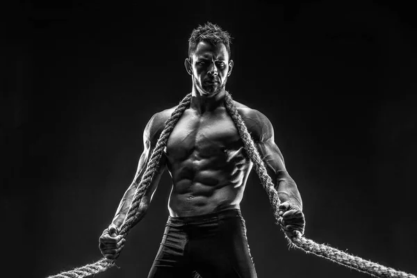 One handsome sexual strong young man with muscular body holding rope with hands hanging on neck and shoulders standing posing in studio on black background — Stock Photo, Image