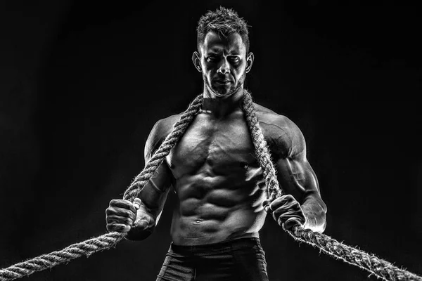 One handsome sexual strong young man with muscular body holding rope with hands hanging on neck and shoulders standing posing in studio on black background — Stock Photo, Image